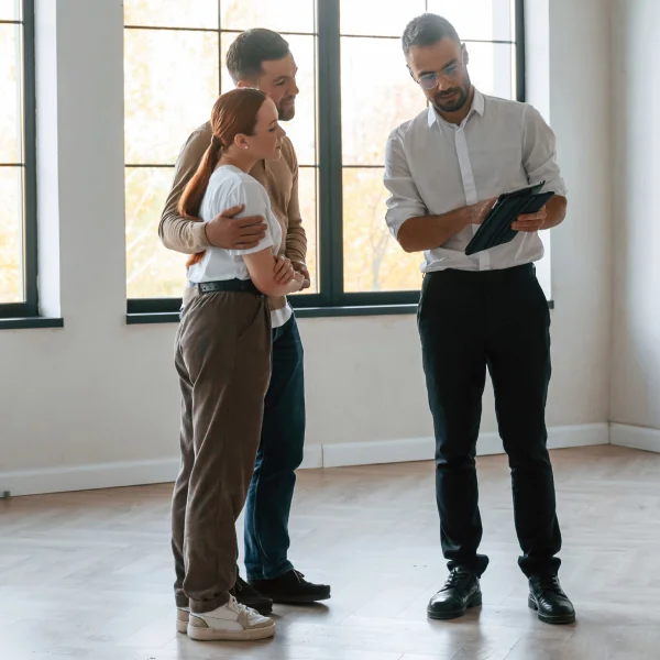 Trois personnes se tiennent dans une pièce vide, tenant une tablette pour une évaluation immobilière.