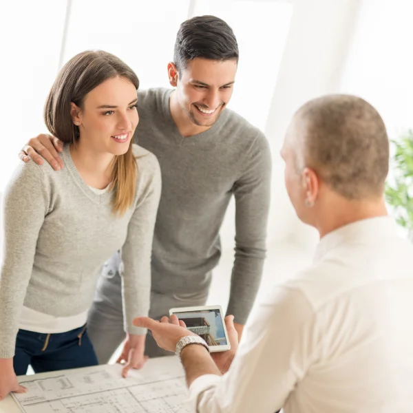 Un homme et une femme regardent une tablette, tandis qu'un autre homme se tient à côté d'eux, évaluateur agréé maison.