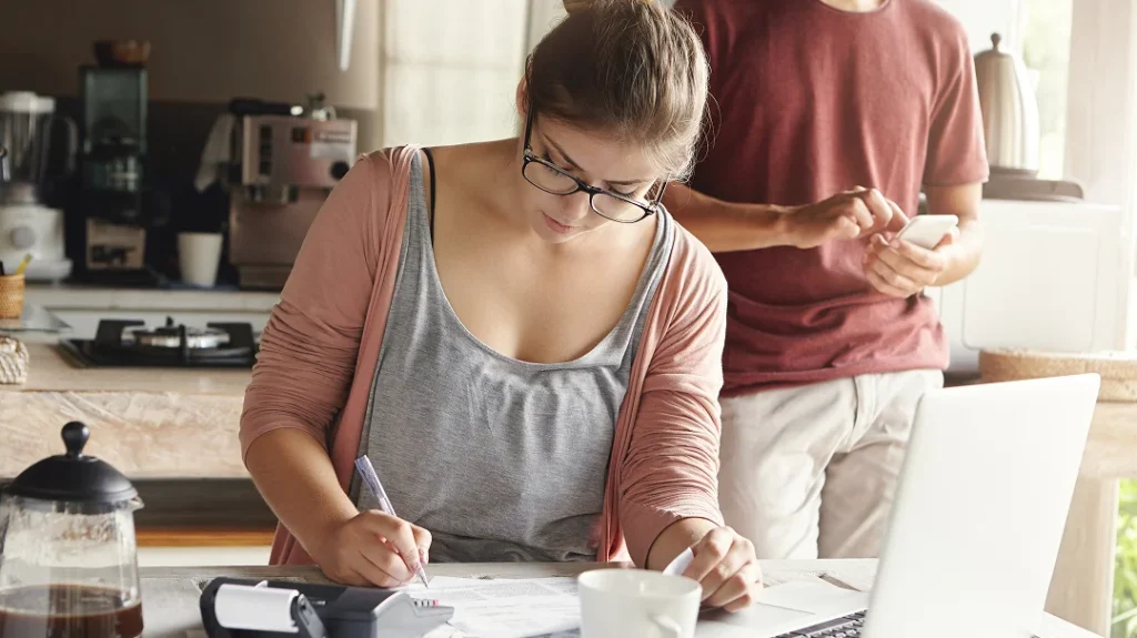 Une femme et un homme examinent des documents devant un ordinateur portable, discutant de l'évaluation de leur maison.