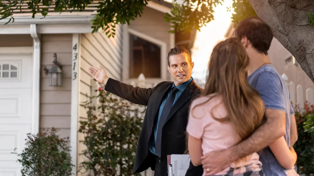 Un homme et une femme devant une maison, l'homme pointe quelque chose en discutant de l'évaluation de la maison.